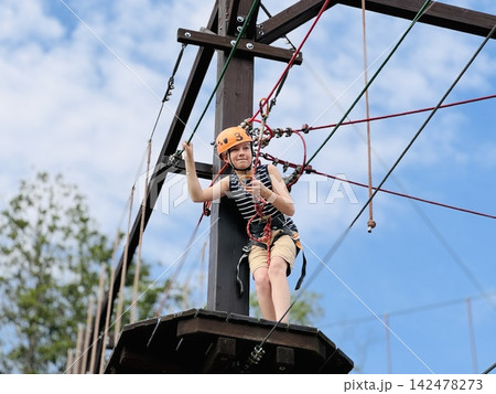 a teenage boy standing on wooden platfoirm in outdoor rope park climbing on obstacle course. 142478273