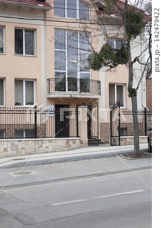 Building with a fence is located on a street in a city on a cloudy day Building with a fence is located on a street in a city on a cloudy day 142479422