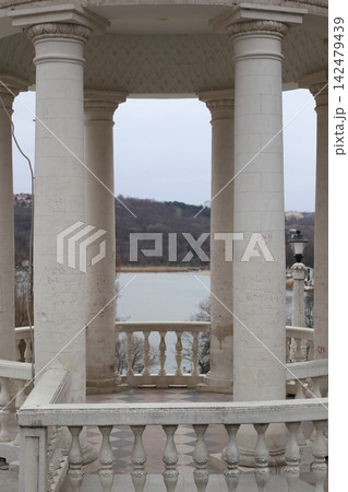 A structure with tall white columns overlooks a body of water. 142479439