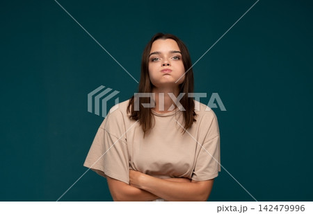Young woman puffing cheeks, showing frustration and impudence, feeling annoyed and sulky with folded arms Young woman puffing cheeks, showing frustration and impudence, feeling annoyed and sulky with folded arms 142479996