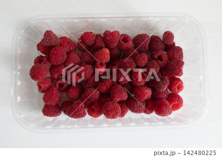 Fresh raspberries packed in a transparent plastic food container on a white background. Top view of red ripe berries for food packaging, grocery, retail and healthy eating concepts Fresh raspberries packed in a transparent plastic food container on a white background. Top view of red ripe berries for food packaging, grocery, retail and healthy eating concepts 142480225