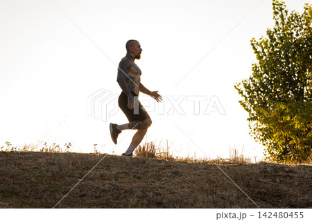 Man runs on a hillside during sunset while wearing shorts and shoes 142480455