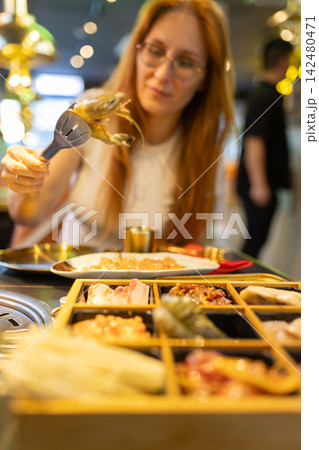 Woman cooking shrimp at korean barbecue restaurant Woman cooking shrimp at korean barbecue restaurant 142480471