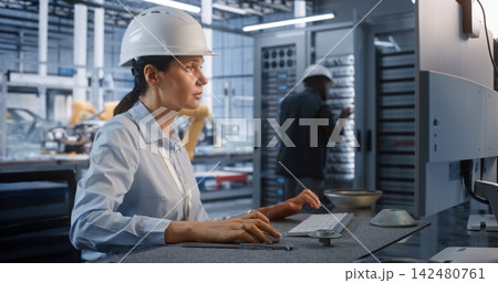 Female Technician Operating Computer Workstation near Server Rack in Plant Female Technician Operating Computer Workstation near Server Rack in Plant 142480761