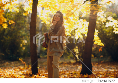 Smiling young woman walking in autumn forest with the yellow leaves at sunset. 142481577