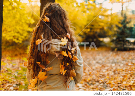 Young woman with the yellow leaves in her hair standing in the autumn park Young woman with the yellow leaves in her hair standing in the autumn park 142481596