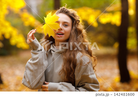 Young woman holds yellow leaf in her hand with smile in the park at sunset. Young woman holds yellow leaf in her hand with smile in the park at sunset. 142481600