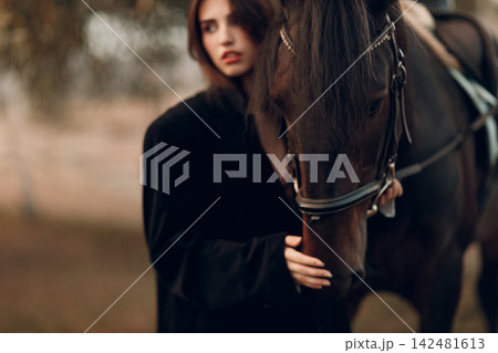 Young woman in black with her horse at sunset outdoors. Young woman in black with her horse at sunset outdoors. 142481613