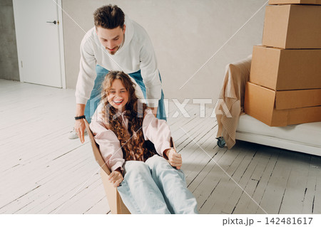Happy young family couple man carry woman inside box. Moving with cardboard boxes to new estate home apartment concept. Happy young family couple man carry woman inside box. Moving with cardboard boxes to new estate home apartment concept. 142481617