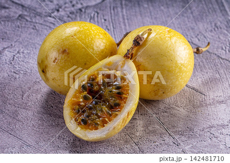 Ripe yellow passion fruit with one cut open on grey textured surface Ripe yellow passion fruit with one cut open on grey textured surface 142481710