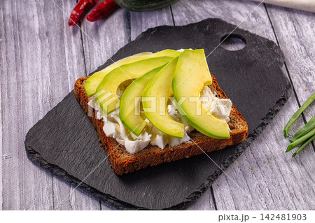 Healthy avocado toast with cream cheese on dark rye bread on slate platter 142481903