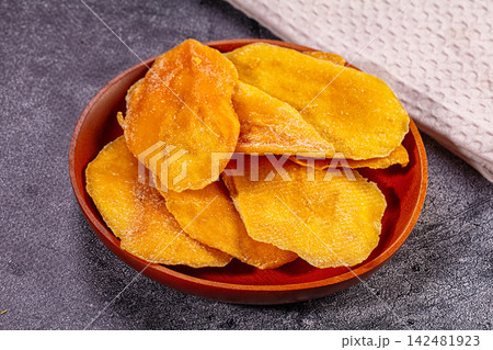 Dried mango slices in a wooden bowl on a dark textured background Dried mango slices in a wooden bowl on a dark textured background 142481923