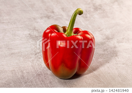 Single red bell pepper with green stem on a textured stone background Single red bell pepper with green stem on a textured stone background 142481940