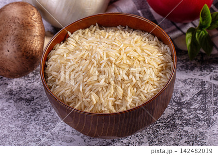 Uncooked basmati rice in wooden bowl with mushroom garlic tomato and basil on textured surface Uncooked basmati rice in wooden bowl with mushroom garlic tomato and basil on textured surface 142482019