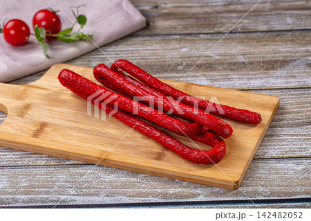 Mini salami sausages on wooden cutting board with cherry tomatoes 142482052