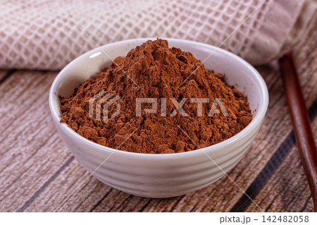 Cocoa powder in white ceramic bowl on rustic wooden surface Cocoa powder in white ceramic bowl on rustic wooden surface 142482058