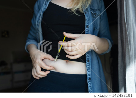 Woman making hormone injection into belly at home for ivf fertility treatment and ovulation stimulation. Concept of reproductive medicine, hormone therapy, and subcutaneous injection. 142482191