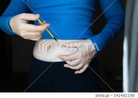 Woman making hormone injection into belly at home for ivf fertility treatment and ovulation stimulation. Concept of reproductive medicine, hormone therapy, and subcutaneous injection. 142482198