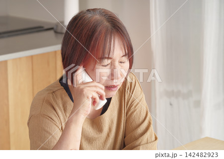 受話器を握りしめて電話するシニア女性 受話器を握りしめて電話するシニア女性 142482923