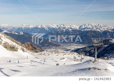 Kaprun ski resort spreads across snowy alpine slopes with chairlifts, pistes and dramatic mountain panorama. Winter landscape reveals Austrian Alps, valley scenery and active skiing tourism 142482963
