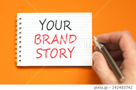Branding and your brand story symbol. Concept words Your brand story on beautiful white note. Beautiful orange background. Businessman hand. Business branding your brand story concept. Copy space. 142483742