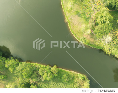Drone view of curving lake water framed by green shoreline in tropical landscape. Water sustainability, conservation, ecosystem care, and nature themes. Environmental conservation. Land management. Drone view of curving lake water framed by green shoreline in tropical landscape. Water sustainability, conservation, ecosystem care, and nature themes. Environmental conservation. Land management. 142483883