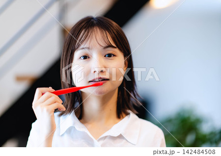 赤い歯ブラシで歯を磨くカメラ目線の若い日本人女性 赤い歯ブラシで歯を磨くカメラ目線の若い日本人女性 142484508