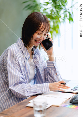 スマートフォンで通話しながらノートパソコンで働く笑顔の女性 スマートフォンで通話しながらノートパソコンで働く笑顔の女性 142484519