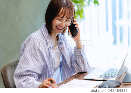 スマートフォンで楽しく通話する笑顔の若い女性とノートパソコン 142484522