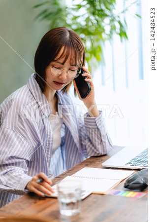 スマートフォンで通話しながらノートにメモを取る若い女性 スマートフォンで通話しながらノートにメモを取る若い女性 142484523