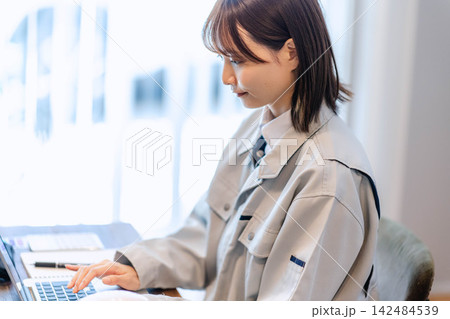 作業着姿でパソコン入力をする若い女性作業員 作業着姿でパソコン入力をする若い女性作業員 142484539
