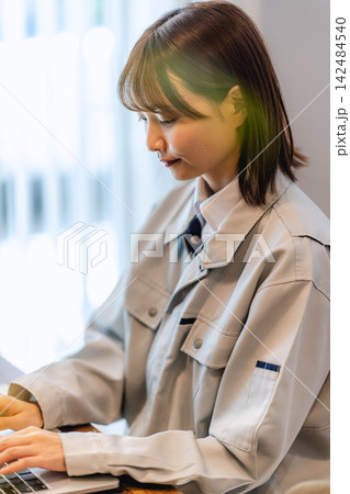作業着姿でノートパソコンに向かう若い女性作業員 142484540