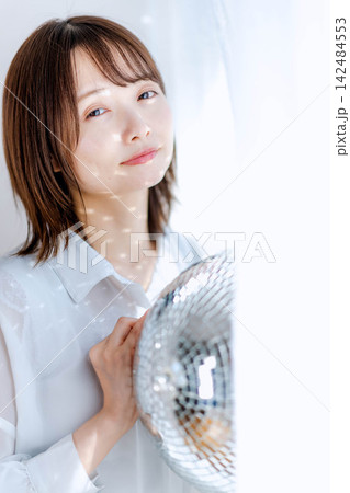 ミラーボールを持ち微笑む白いブラウスの女性 142484553