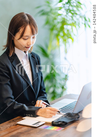 スーツ姿でノートにメモを取りながら働く若い女性 スーツ姿でノートにメモを取りながら働く若い女性 142484588