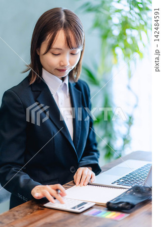 スーツ姿で電卓を使い計算をする若い女性 スーツ姿で電卓を使い計算をする若い女性 142484591