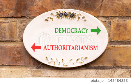 Democracy or authoritarianism symbol. Concept words Democracy Authoritarianism on beautiful white sign plate. Beautiful brick wall background. Business democracy authoritarianism concept. Copy space Democracy or authoritarianism symbol. Concept words Democracy Authoritarianism on beautiful white sign plate. Beautiful brick wall background. Business democracy authoritarianism concept. Copy space 142484828