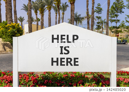 Help is here and support words symbol. Concept words Help is here on beautiful white road sign. Beautiful palm trees background. Business help is here and support concept. Copy space. 142485020