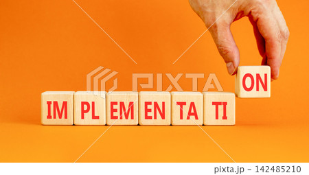 Implementation word symbol. Concept word Implementation on beautiful wooden blocks. Beautiful orange table orange background. Businessman hand. Business implementation word concept. Copy space. Implementation word symbol. Concept word Implementation on beautiful wooden blocks. Beautiful orange table orange background. Businessman hand. Business implementation word concept. Copy space. 142485210