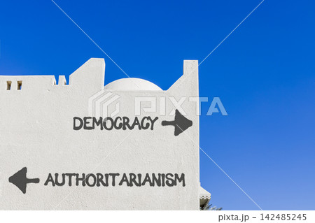 Democracy or authoritarianism symbol. Concept words Democracy Authoritarianism on beautiful white wall. Beautiful blue sky background. Business democracy authoritarianism concept. Copy space Democracy or authoritarianism symbol. Concept words Democracy Authoritarianism on beautiful white wall. Beautiful blue sky background. Business democracy authoritarianism concept. Copy space 142485245