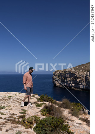 Traveler walking on a high rocky cliff edge with a scenic sea and bay view in Malta. Traveler walking on a high rocky cliff edge with a scenic sea and bay view in Malta. 142487947