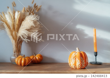 Cozy warm autumn home interior - decorative orange ceramic pumpkins, candles, dried flowers on the wooden console with white wall background. Scandinavian minimalist hygge home fall decor Cozy warm autumn home interior - decorative orange ceramic pumpkins, candles, dried flowers on the wooden console with white wall background. Scandinavian minimalist hygge home fall decor 142488413