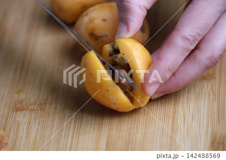 Slicing fresh fruit. Hand holding loquats. Yellow fruit hand. medlar in hand, close-up. High quality photo Slicing fresh fruit. Hand holding loquats. Yellow fruit hand. medlar in hand, close-up. High quality photo 142488569