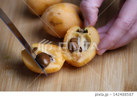Slicing fresh fruit. Hand holding loquats. Yellow fruit hand. medlar in hand, close-up. High quality photo Slicing fresh fruit. Hand holding loquats. Yellow fruit hand. medlar in hand, close-up. High quality photo 142488587