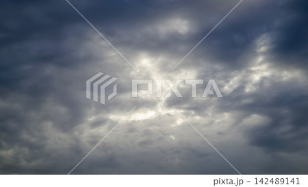 heavy grey clouds centered with a bright sunlit gap glowing through the dark sky 142489141