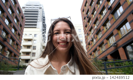 Portrait of an attractive woman with a beautiful smile and long hair against the backdrop of a residential area on a summer day. 142489512