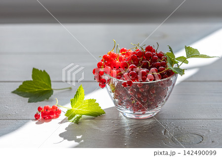 Fresh red currants overflowing a glass bowl on a wooden table Fresh red currants overflowing a glass bowl on a wooden table 142490099