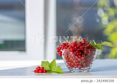 Fresh red currants overflowing a glass bowl on white table 142490100