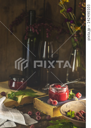 Raspberry jam with wine and old books on wooden table 142490103