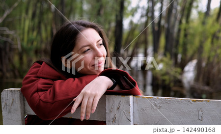 Portrait photo of beautiful young smiling woman in burgundy coat sitting on bench outdoors in park. Portrait photo of beautiful young smiling woman in burgundy coat sitting on bench outdoors in park. 142490168