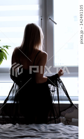 A sexy beautiful woman in a black erotic negligee stands near the window in the bedroom. A sexy beautiful woman in a black erotic negligee stands near the window in the bedroom. 142491105